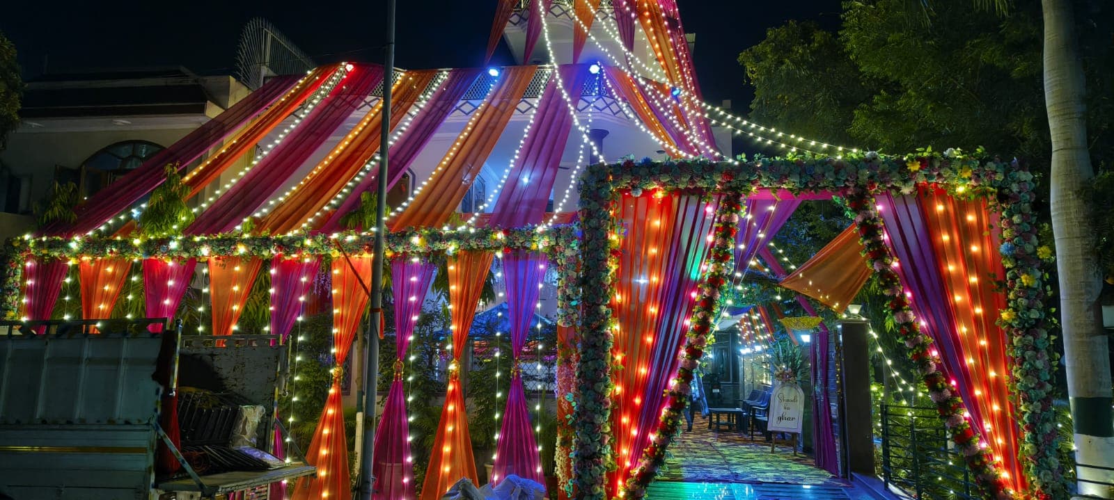 Grand illuminated evening wedding entrance gateway with silk drapes, stage lighting and floral borders in Greater Noida
